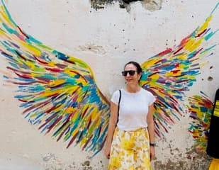 Sandra Hodes standing in front of a colorful wings mural