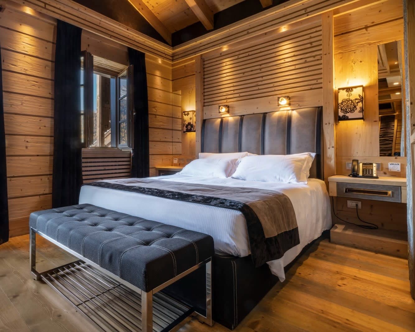 modern bedroom with white sheets, black and grey accent furniture and tan wood floors and walls