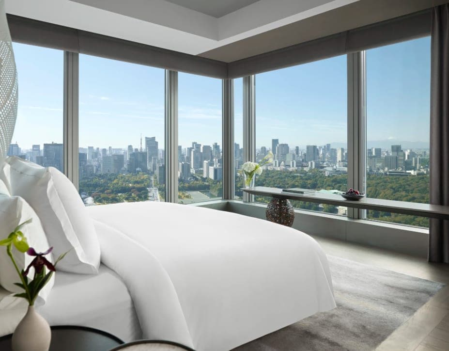 A modern corner suite with floor-to-ceiling windows overlooking Tokyo’s skyline and a city park.